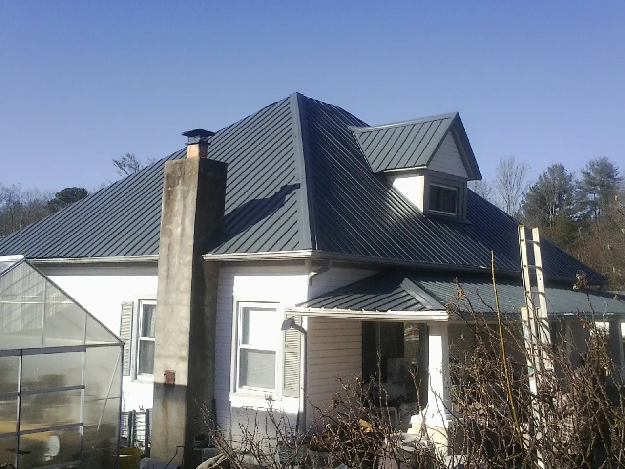 Dark blue standing seam metal roof on a white farmhouse with dormer — Slate & Tile Roof Repair by Roofing Brothers in Sisters