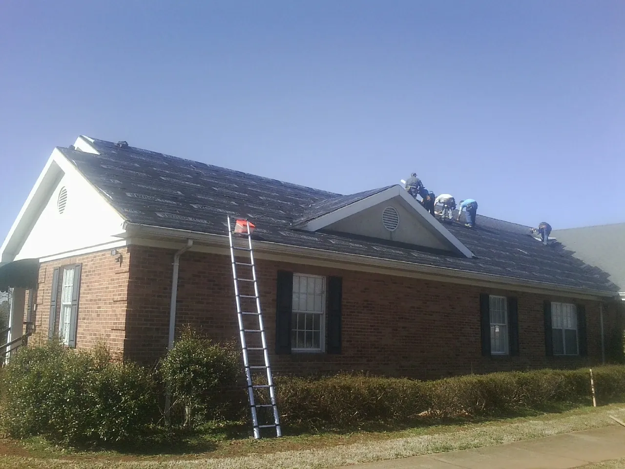 Crew tearing shingles off a brick ranch roof with a ladder set — Metal Roof Repair work by our crew in Sisters