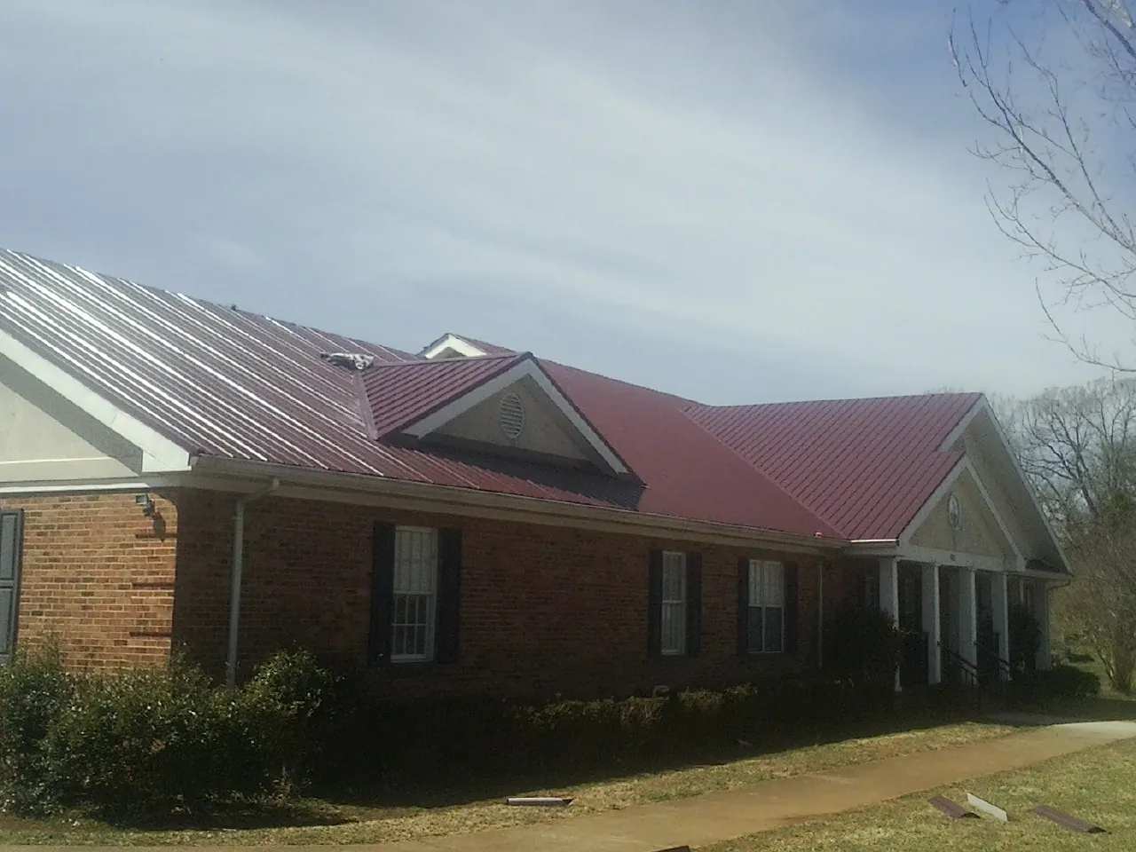 Red metal roof with gabled entries on a long brick building, from a Hail Damage Roof Repair job in Sisters