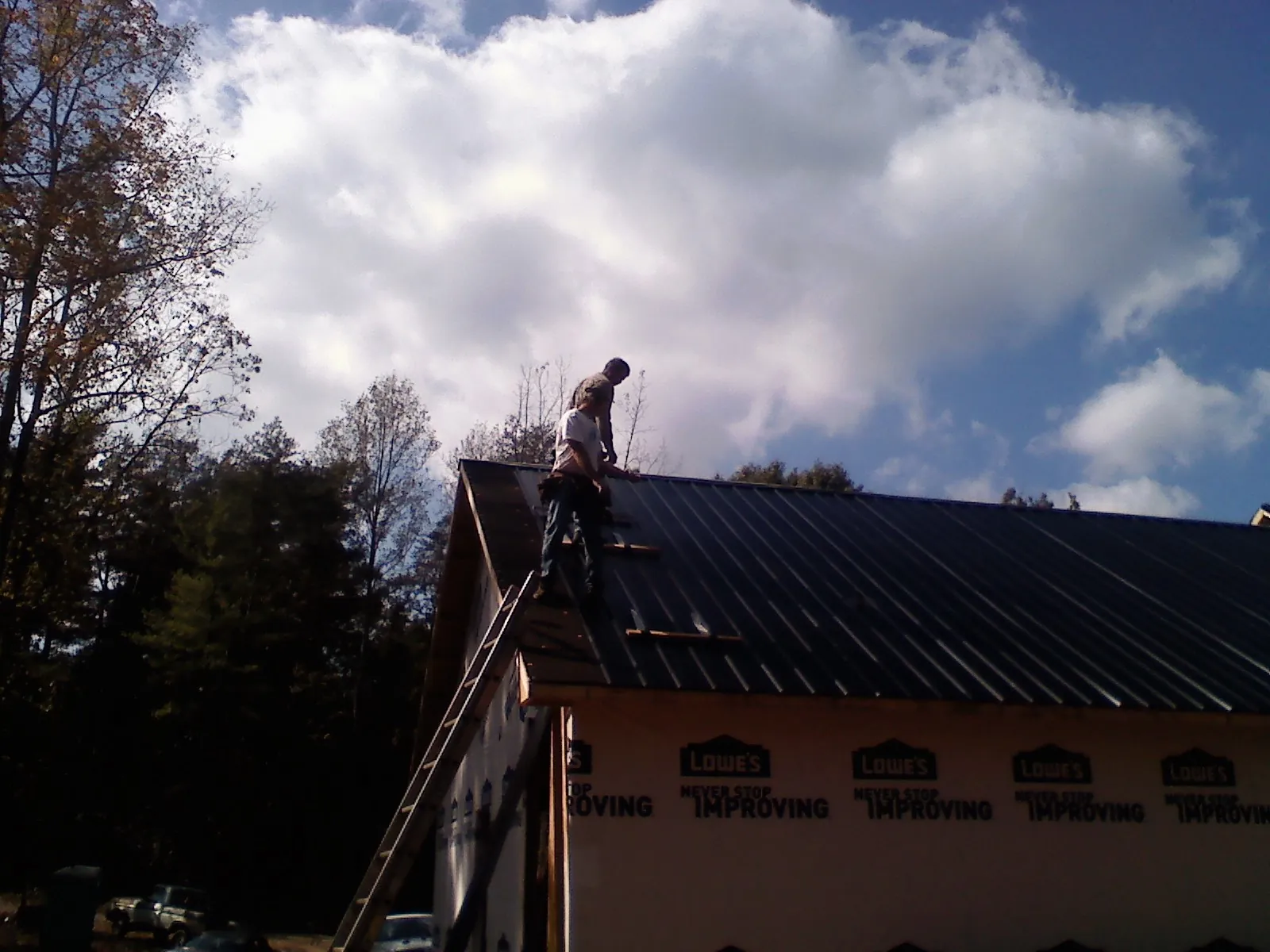 Roofer fastening dark metal panels high against a cloudy sky, from a Roof Inspection job in Sisters
