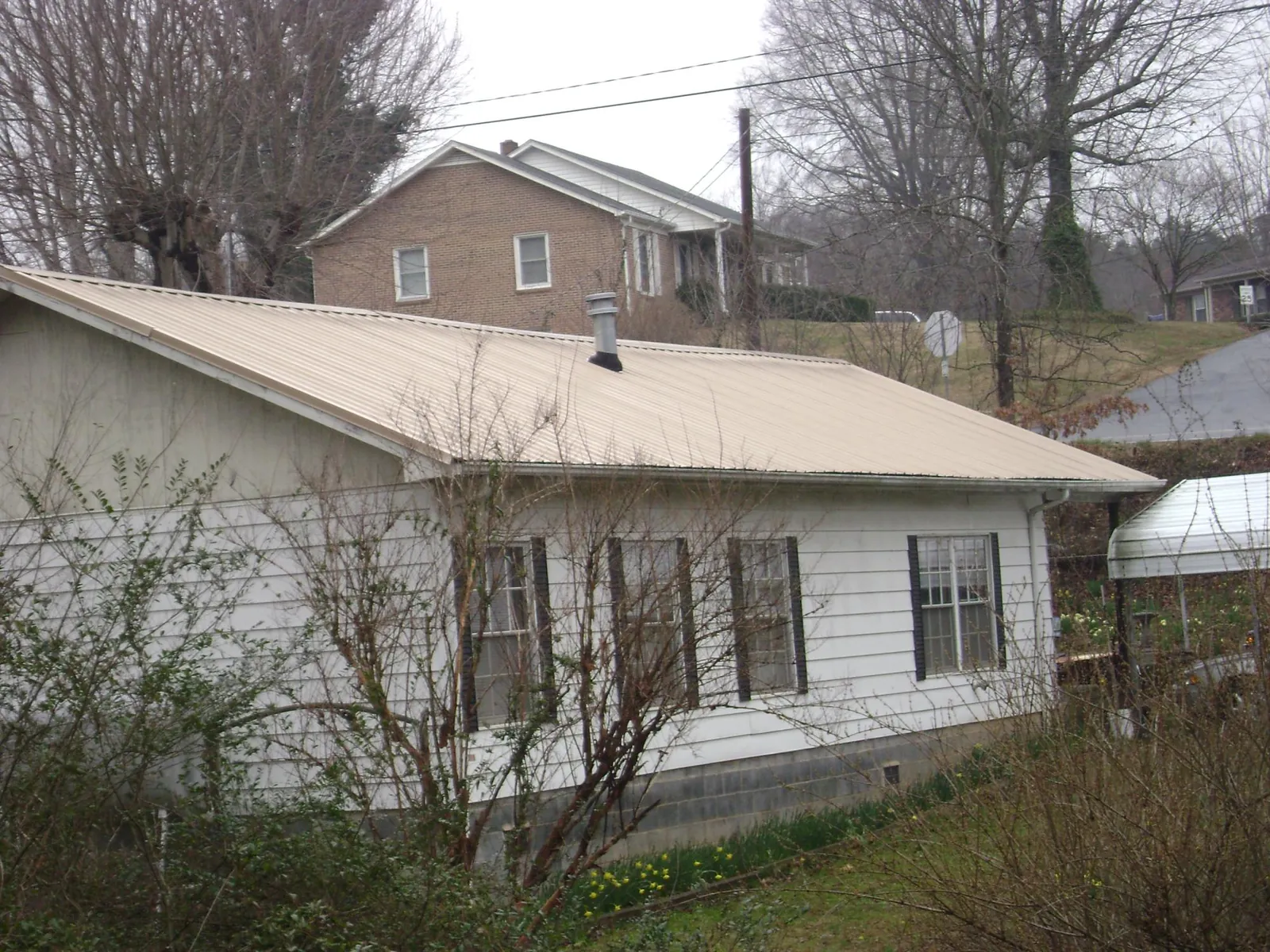 Tan metal roof on a white sided house set into a hillside — Commercial Roofing by Roofing Brothers in Sisters